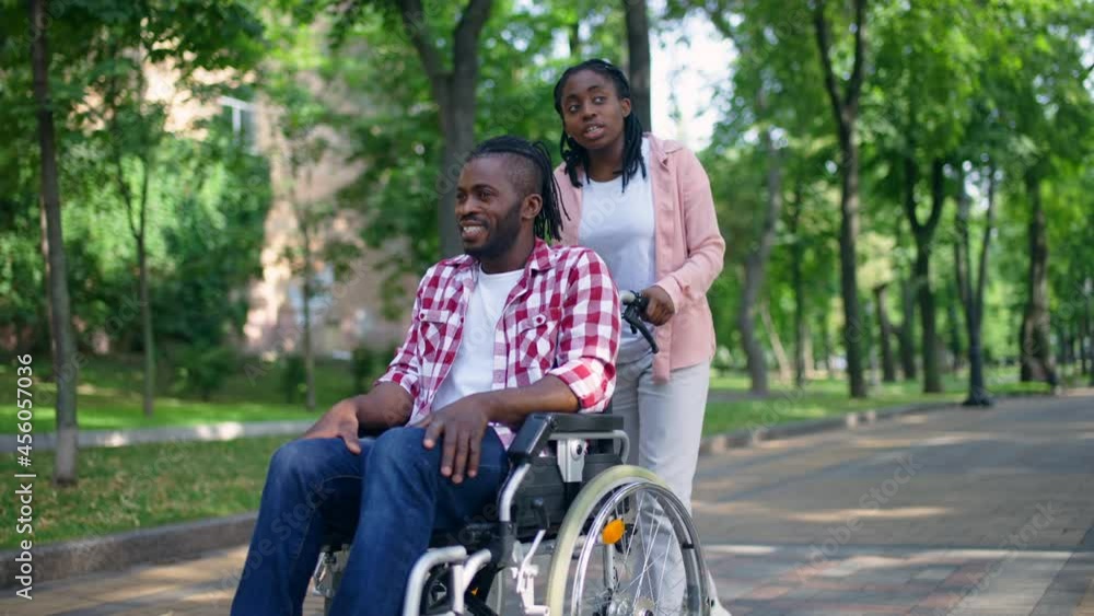 Black nurse pushing wheelchair with male patient in hospital park, recovery Black nurse pushing wheelchair with male patient in hospital park, recovery