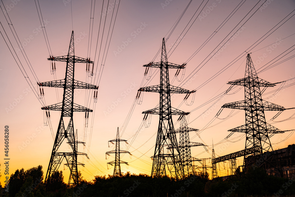 Dark silhouettes of electric towers on red sky background. Transmission lines of high-voltage electric towers at sunset