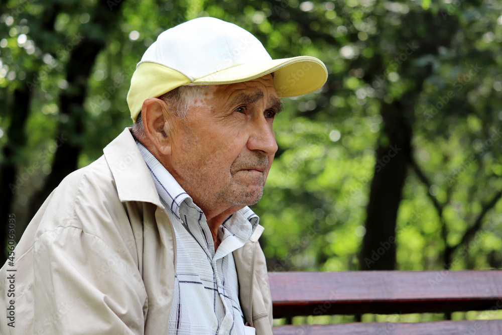 Portrait of pensive elderly man sitting on a bench in a green park. Concept of life in village, old age Portrait of pensive elderly man sitting on a bench in a green park. Concept of life in village, old age