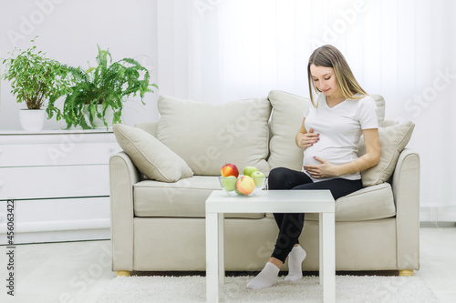 Photo of young woman touching her stomach on sofa.