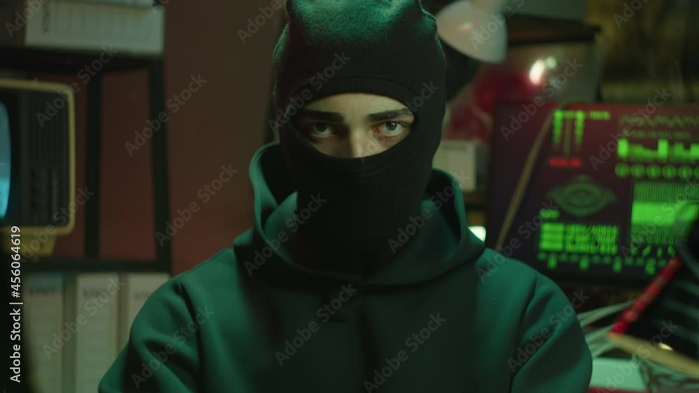 Hacker wearing balaclava portrait, looking in camera. Stealing information, breaking password. Young man criminal working with computer system. Professional hacker attack. Hacker wearing balaclava portrait, looking in camera. Stealing information, breaking password. Young man criminal working with computer system. Professional hacker attack.