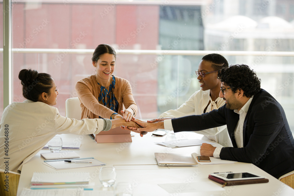 Business people touching hands, celebrating success in conference room