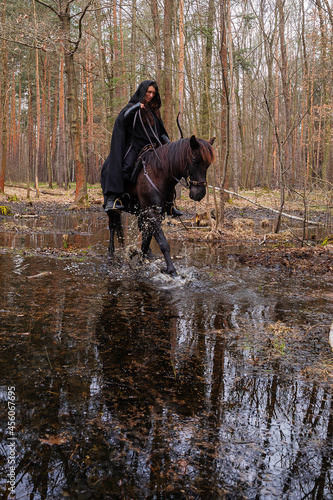 a woman in a historical costume with a bow and arrows riding a horse through a forest swamp