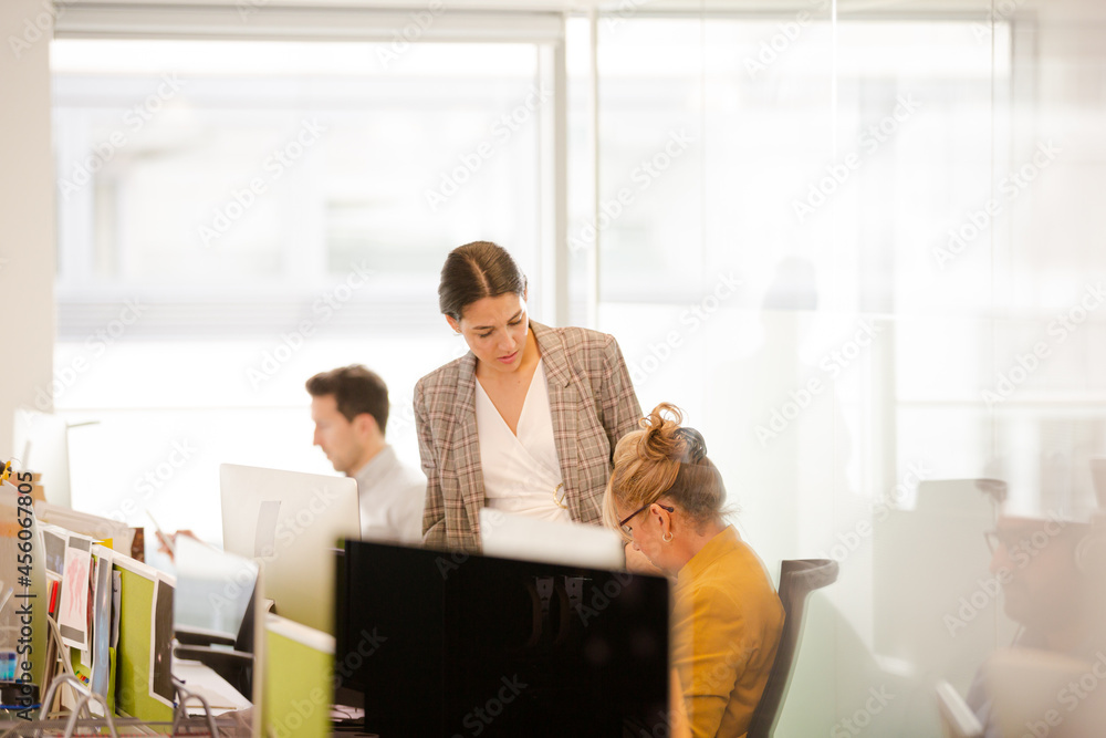 Businesswomen talking at computer in open plan office Businesswomen talking at computer in open plan office