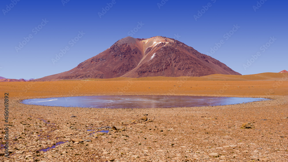 Desolate mountain landscape in the Andes in the north of Chile with volcano and a small frozen lake 
