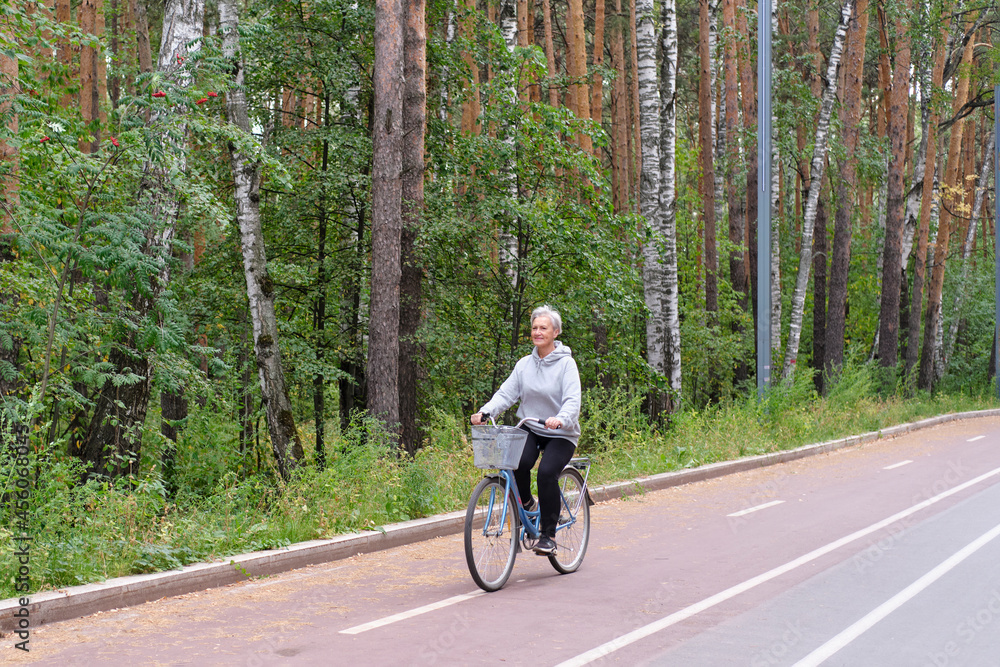 Fototapeta premium Active senior caucasian woman with gray hair is riding bike on bicycle path in forest park.
