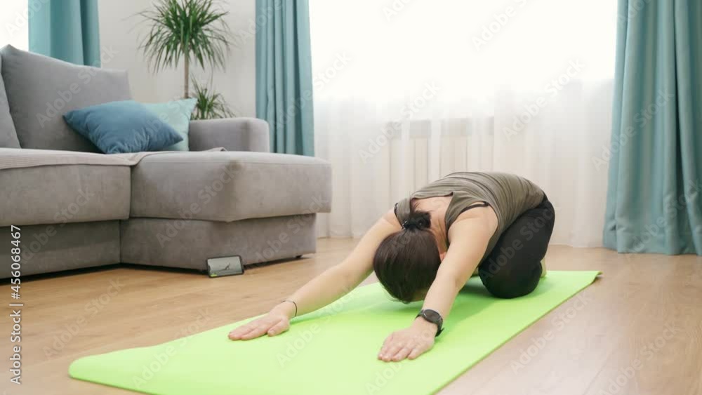 A woman at home performs exercises on a gymnastic mat. The girl uses a mobile application for fitness classes. A woman at home performs exercises on a gymnastic mat. The girl uses a mobile application for fitness classes.