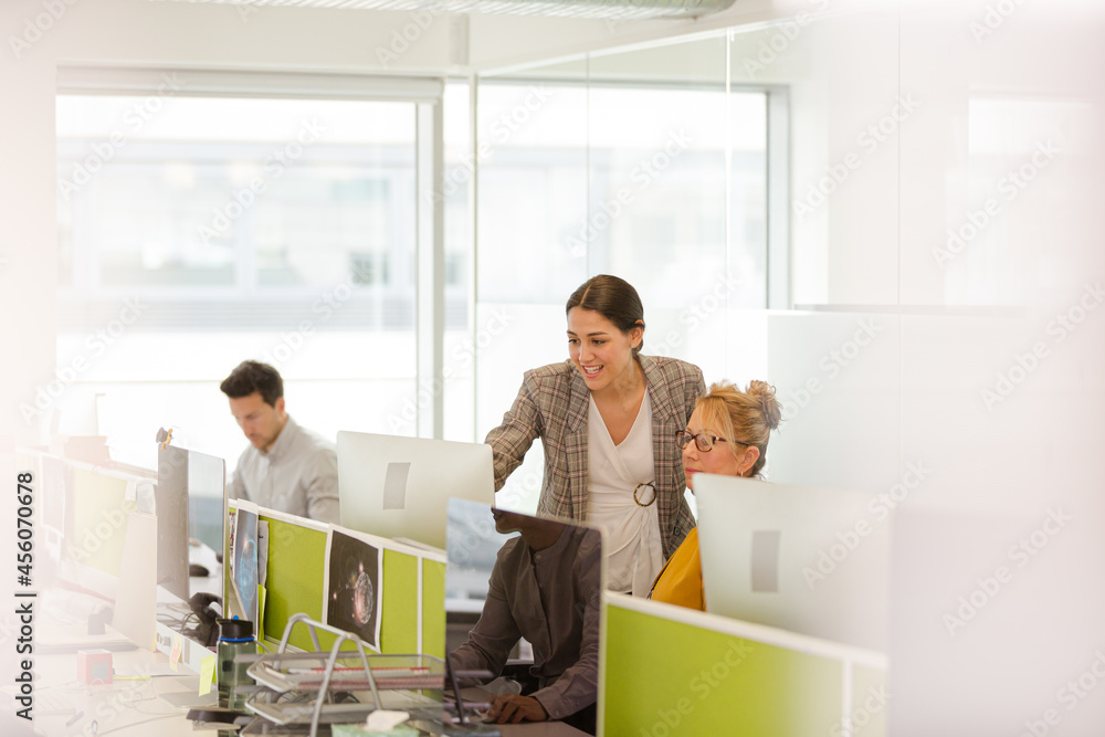 Businesswomen talking at computer in open plan office Businesswomen talking at computer in open plan office