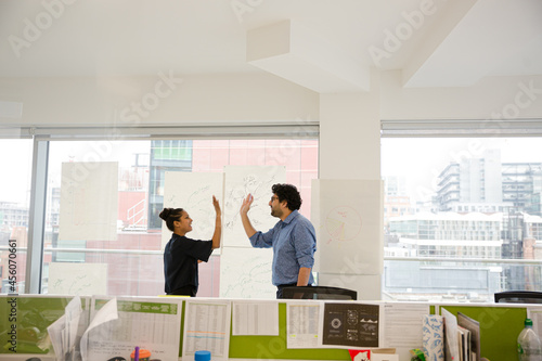 Businessman and businesswoman discussing diagram sketches hanging on conference room window