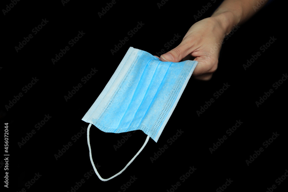 Woman's hand holds out blue facial medical mask on a black background Woman's hand holds out blue facial medical mask on a black background