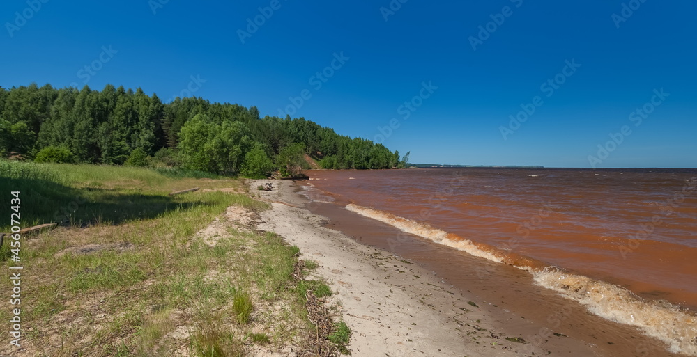 Summer landscape with the river, red from dissolved clay, trees, shrubs on the shore against the blue sky Summer landscape with the river, red from dissolved clay, trees, shrubs on the shore against the blue sky