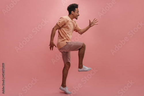 profile photo positive young man with dark skin jumping on pastel background. attractive brunette waving her arms gleefully, dressed in casual shades of pink.