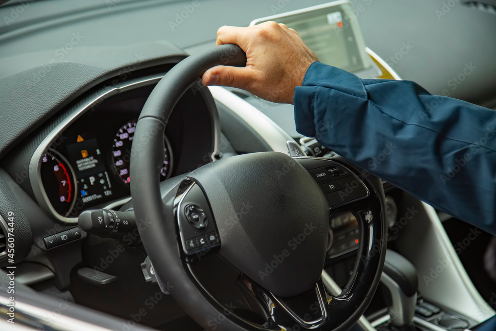 faceless Man sits by wheel of car male hand on steering wheel of a modern car.