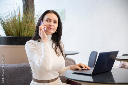 beautiful middle-aged woman smiling talking on the phone at laptop in office