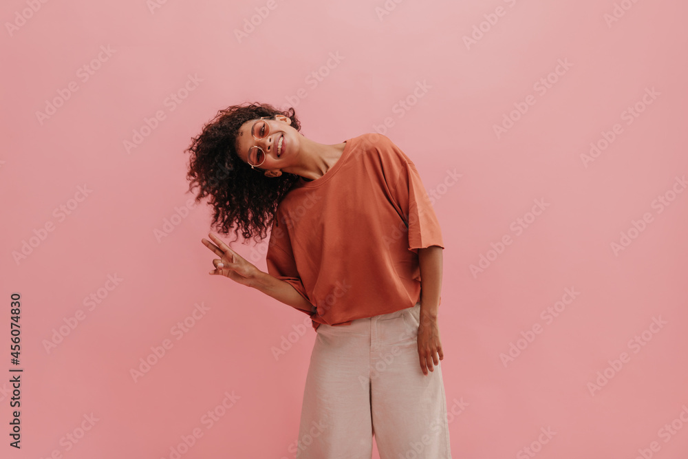 impressive, funny lady in background of studio background tilted head to one side, showing two thumbs up. dark short curly hair flying beautifully in photo. girl in glasses smiles broadly with teeth. impressive, funny lady in background of studio background tilted head to one side, showing two thumbs up. dark short curly hair flying beautifully in photo. girl in glasses smiles broadly with teeth.