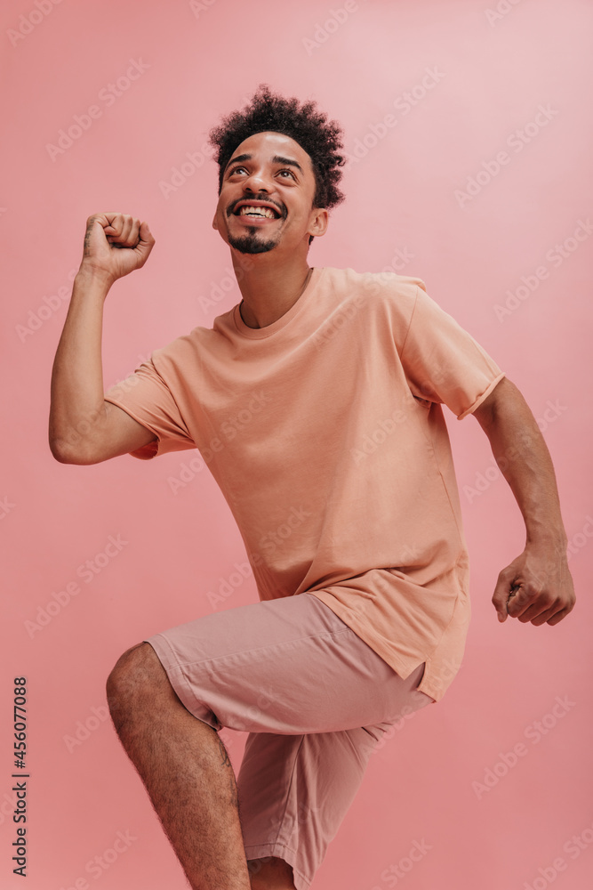 photo of happy black man dancing on pink studio background, copy space. guy with beautifully shaved beard looks up, smiling broadly with his teeth. photo of happy black man dancing on pink studio background, copy space. guy with beautifully shaved beard looks up, smiling broadly with his teeth.