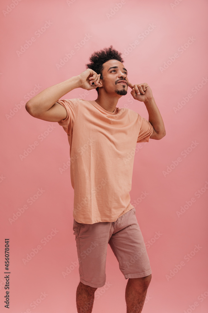 pensive young man holding his head with two hands on pink background. beautifully shaven brunette looks up with concentration. dressed in casual clothes in pastel shades. pensive young man holding his head with two hands on pink background. beautifully shaven brunette looks up with concentration. dressed in casual clothes in pastel shades.
