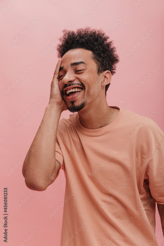 attractive dark-skinned man indoors in pink. handsome man in T-shirt remembers something with smile on his face with his eyes closed. attractive dark-skinned man indoors in pink. handsome man in T-shirt remembers something with smile on his face with his eyes closed.