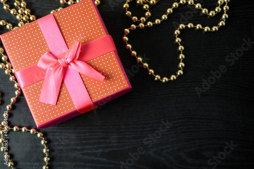 Closeup of red present box with pink ribbon and bow on the black wood