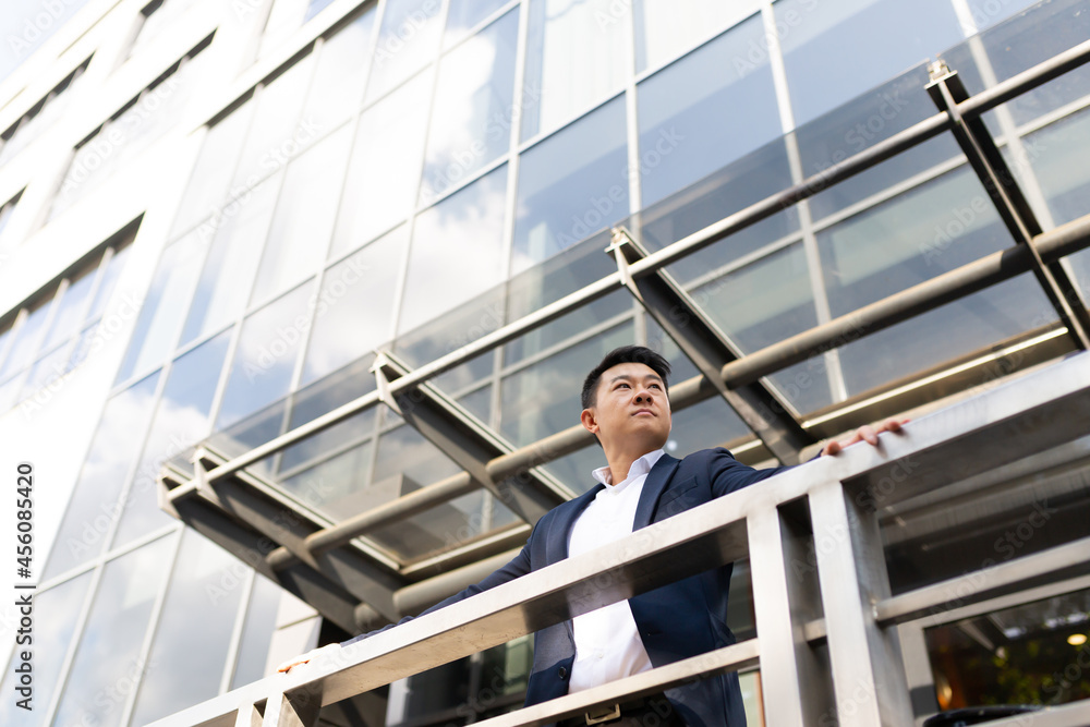 Asian businessman boss stands near his office center on the balcony in a dark color business suit Asian businessman boss stands near his office center on the balcony in a dark color business suit