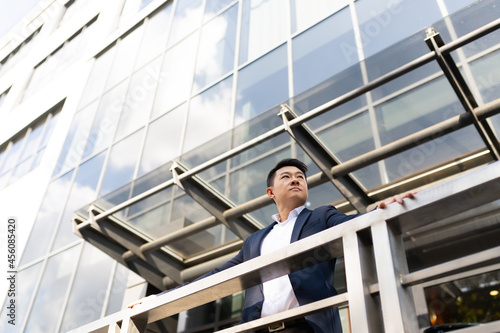 Asian businessman boss stands near his office center on the balcony in a dark color business suit