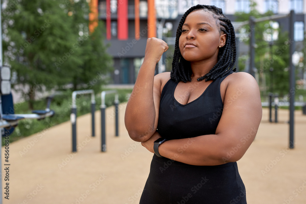 Portrait of young afro american woman in black tracksuit posing at camera, have rest, black fat lady is looking serious and confident, copy space. Sport, healthy lifestyle, workout, fitness concept