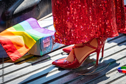 Close up of a drag queen's red stiletto heels, sparkly dress on a pickup truck's bed, with rainbow flag and bracelet during a gay pride celebration.