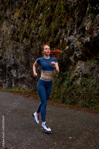 Fitness woman in blue sportive clothes enjoys running jogging in nature, concentrated on correct breathing when running, slim female athlete at street in urban area, spend morning outdoors. copy space © Roman