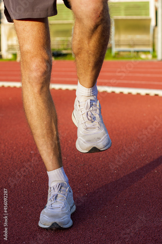 Close up young man runner athlete getting ready to run doing warm up and stretching exercises for muscles of legs before outside training to marathon on athletic field at sunrise time