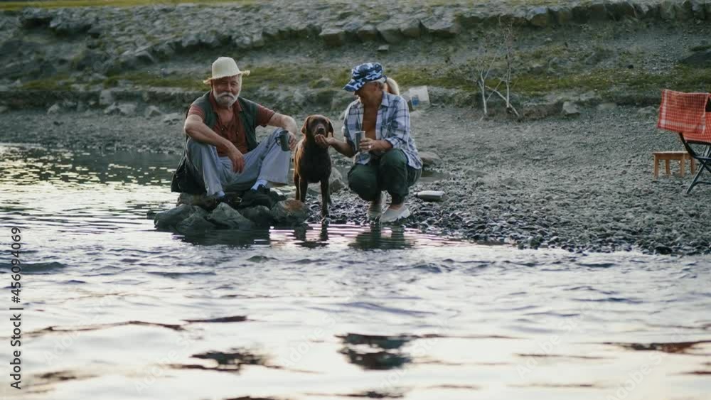 Senior woman gives water from the hands of his dog. Tourist travelers are resting drinking coffee by the stream Senior woman gives water from the hands of his dog. Tourist travelers are resting drinking coffee by the stream