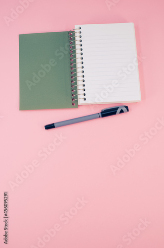 Vertical shot of an open notebook with a penon a pink surface photo