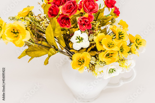 Artificial flowers in the jar. (White background/ high key/ red, white and yellow flowers).
