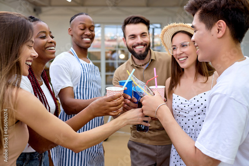 Cheerful diverse friends cheering with lemonade at barbecue dinner party. Multi-ethnic group of Young millennial people having fun at bbq meal outdoor in the evening at summer. Food, fun, youth