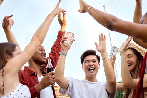 group of excited friends, young diverse men and women doing barbecue in nature, raising hands with beverages, celebrating the end of exams, have fun at picnic, summer time concept, friendship