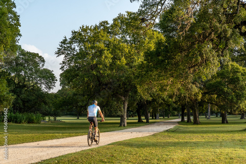 Man, person, rider on a bicycle along a path through a grove of oak trees and grass level area, Swede Creek Park, Cordillera Ranch, Boerne, Hill Country, Texas