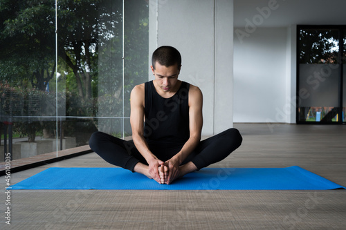 man practicing yoga concept, sitting in baddha konasana exercise in a blue mat
