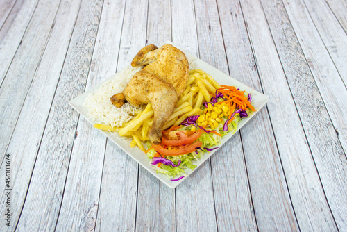 Roast chicken menu with half chicken, french fries, purple cabbage salad with tomato, carrot and sweet corn and white basmati rice on white table