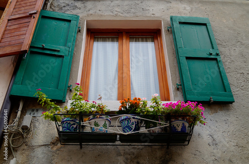a window with green wooden shutters and flowers in flower pots underneath the window in the Italian town of Malcesine