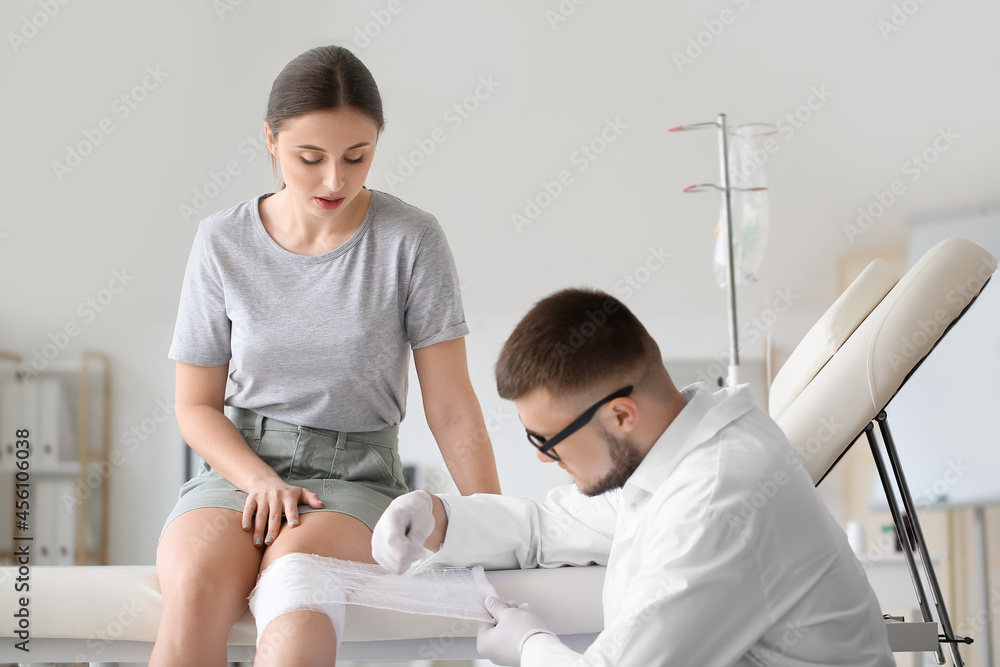 Doctor applying bandage onto knee of young woman in clinic Doctor applying bandage onto knee of young woman in clinic
