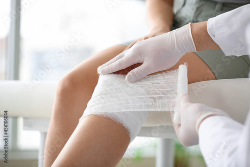 Fototapet Doctor applying bandage onto knee of young woman in clinic