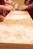 The hands of several people are kneading the dough on the table. Mix a raw egg with flour.