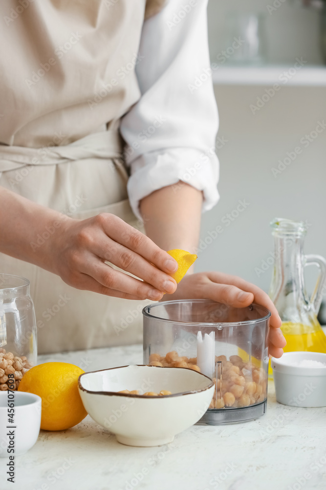 Woman squeezing lemon into blender with chickpeas on table in kitchen, closeup Woman squeezing lemon into blender with chickpeas on table in kitchen, closeup