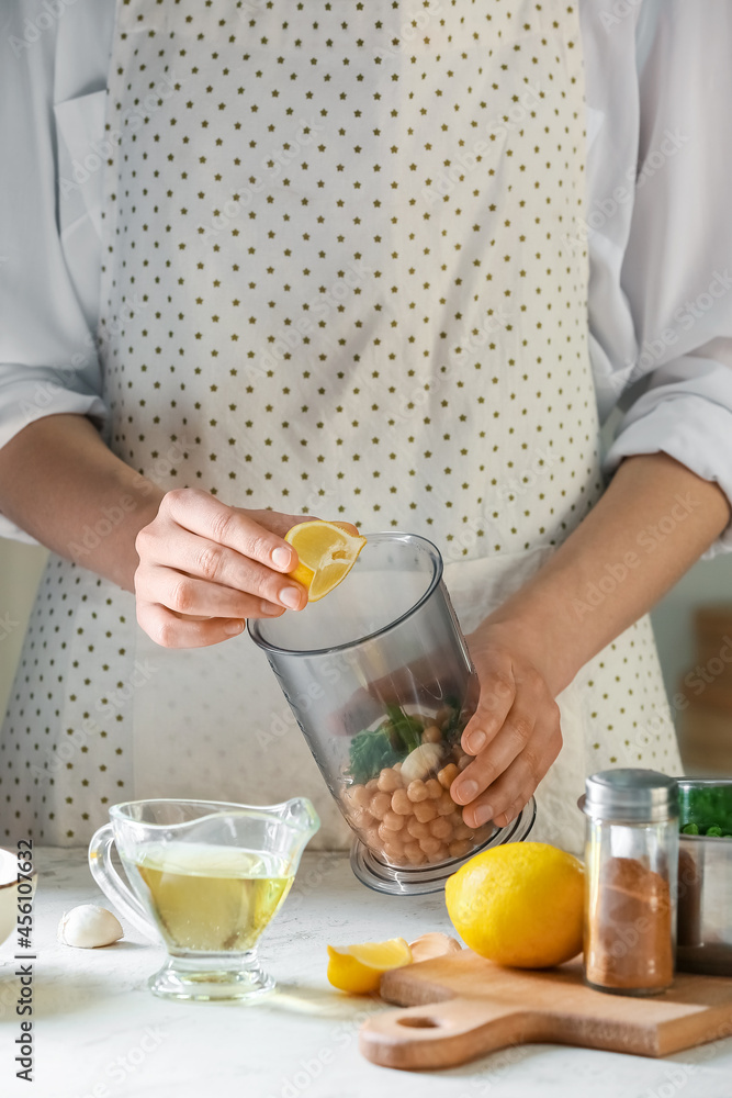 Woman squeezing lemon into blender with chickpeas on table in kitchen, closeup Woman squeezing lemon into blender with chickpeas on table in kitchen, closeup
