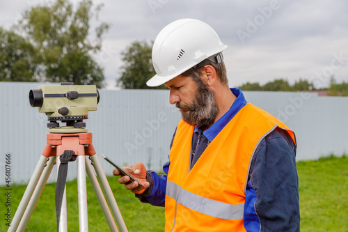 Canvas Print A civil engineer with an optical level looks into a mobile phone.