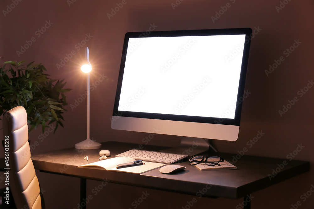 Modern workplace with computer and glowing lamp in dark room Modern workplace with computer and glowing lamp in dark room
