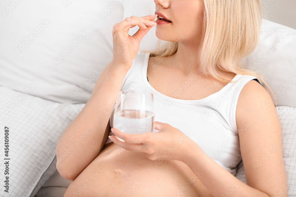 Young pregnant woman taking pill in bedroom Young pregnant woman taking pill in bedroom