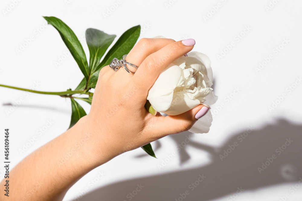 Woman with beautiful manicure and stylish jewelry holding flower on white background