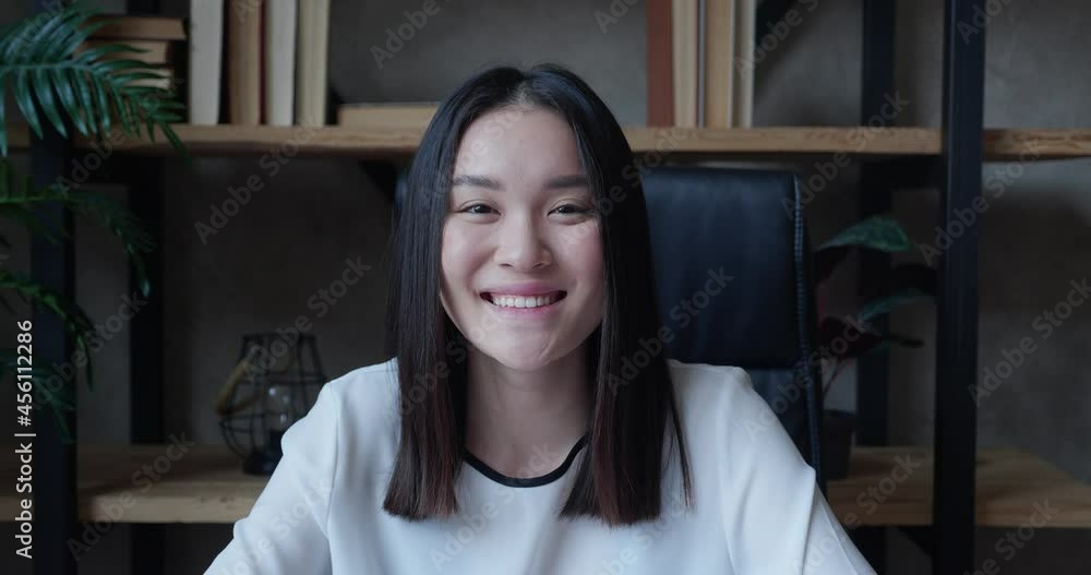 Close-up portrait of attractive cute successful confident young brunette asian woman, office manager, in formal stylish shirt, sits against blurred office background, looks at camera, smiling friendly Close-up portrait of attractive cute successful confident young brunette asian woman, office manager, in formal stylish shirt, sits against blurred office background, looks at camera, smiling friendly
