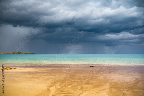 A small stream flowing out to sea over a sandy beach with dark storm clouds and rain over the ocean