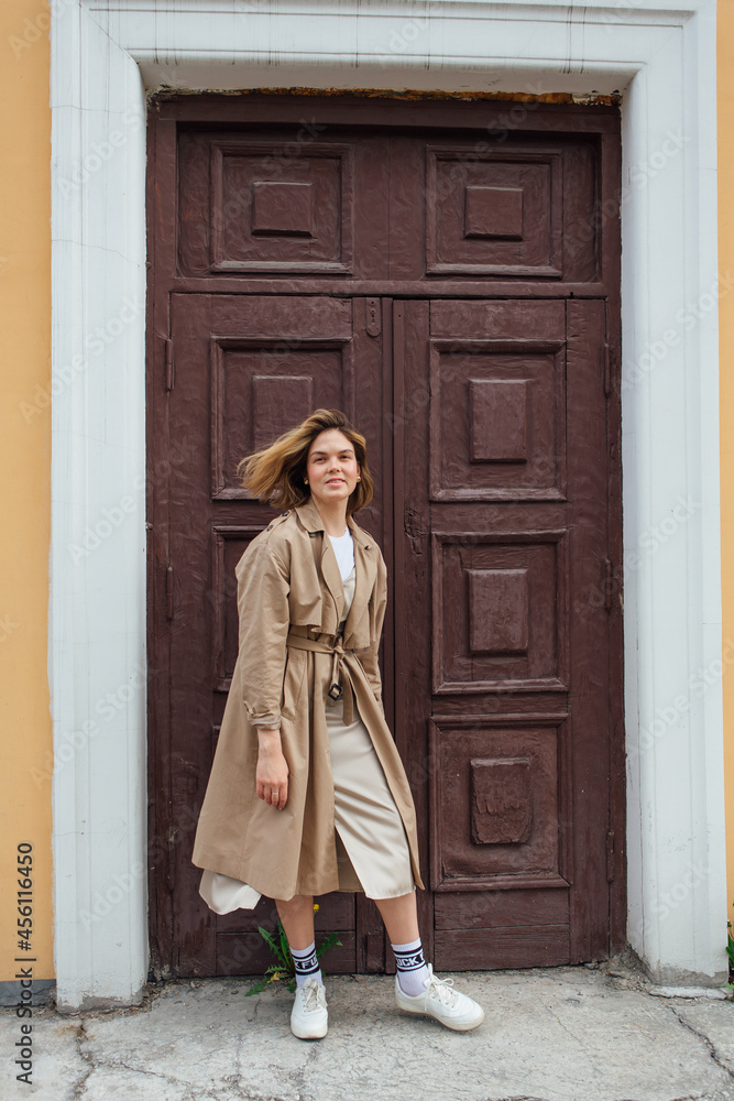 Young millennial woman with wild hair dressed in an autumn coat posing near the door of an old building.